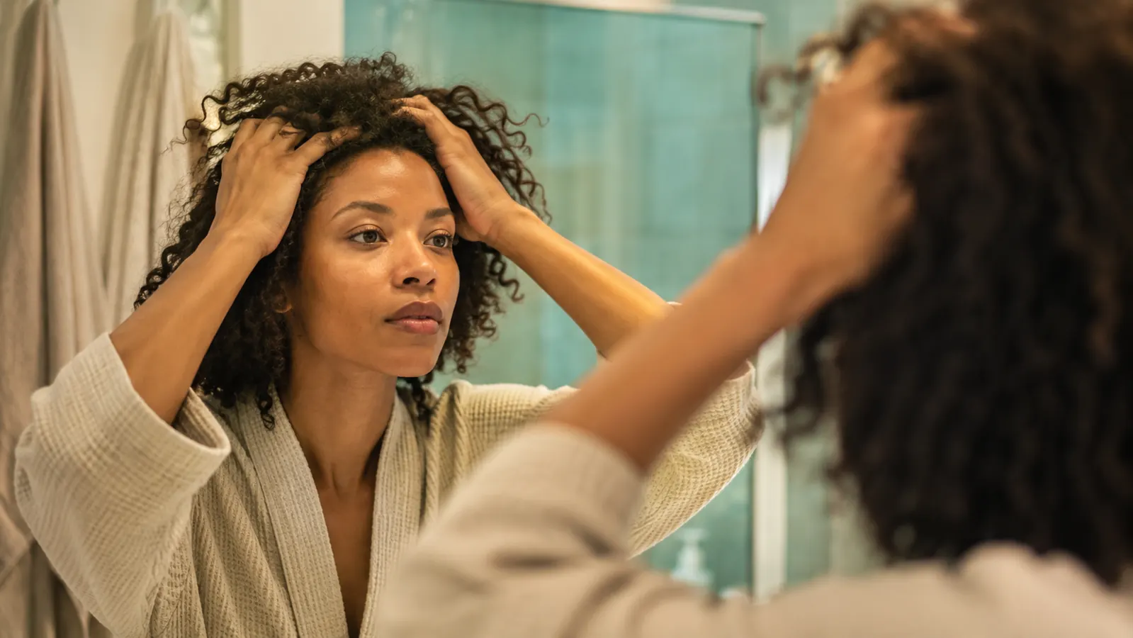 Person massaging rosemary oil into their scalp while looking in a bathroom mirror